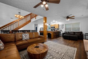 Uma sala de estar espaçosa com um sofá de couro marrom, uma mesa de centro de madeira e uma escada que leva a um andar superior.