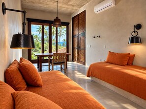 A room with two beds, a dining table, and chairs. There is a view of palm trees and the ocean through large windows. - Casa Apsara: 3-Bedroom Beachfront Villa on Rare Coastline (Zihuatanejo)