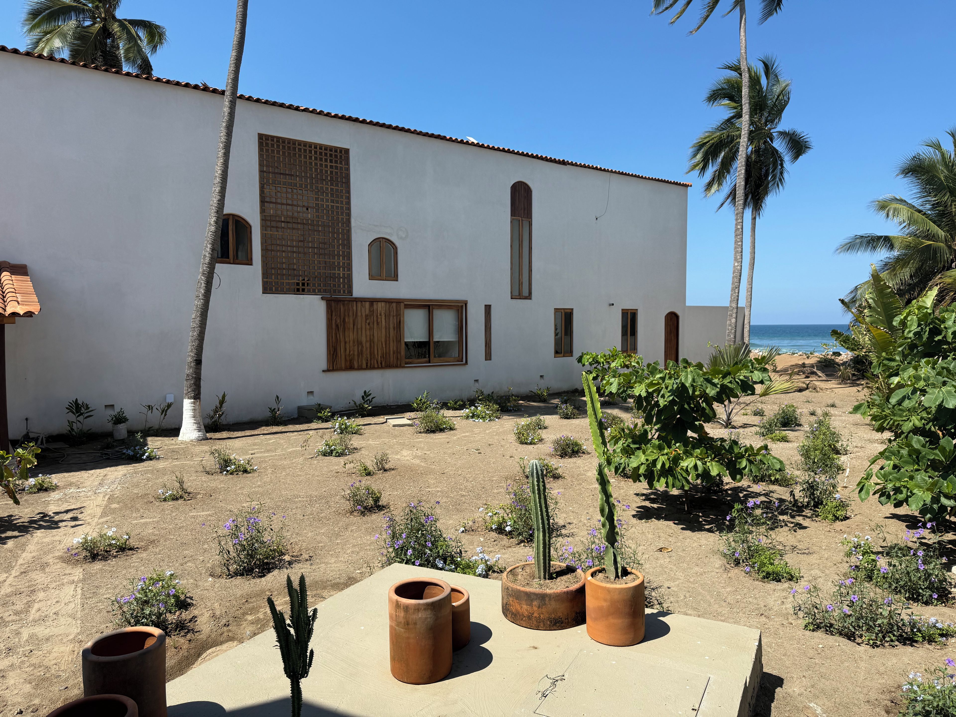 A building with a white exterior, a tiled roof, and a garden with various plants and flowers.