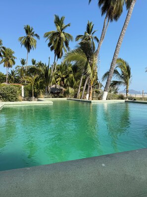 A swimming pool surrounded by palm trees and a clear blue sky. - Casa Apsara: 3-Bedroom Beachfront Villa on Rare Coastline (Zihuatanejo)