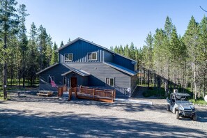Une cabane à deux étages avec une terrasse en bois et un véhicule garé à proximité.