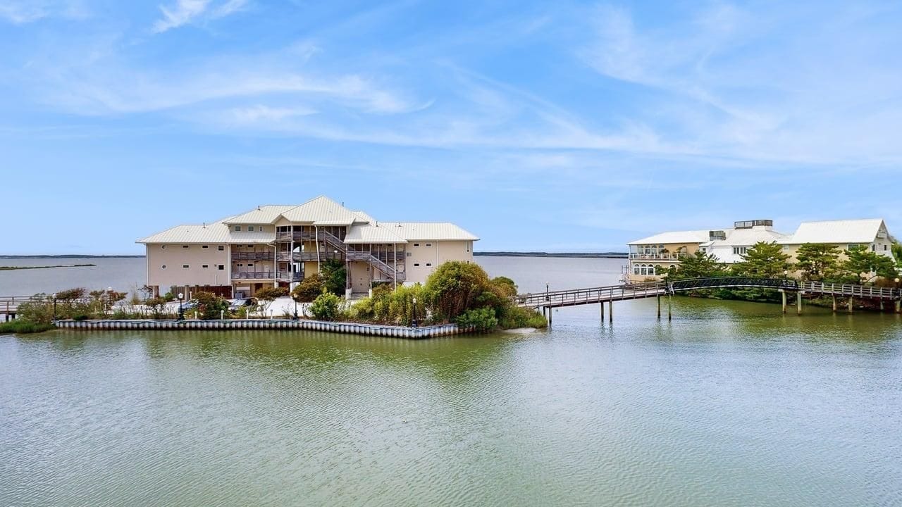 A waterfront property with a large building featuring multiple floors and balconies, a dock, and a small island with a fence.