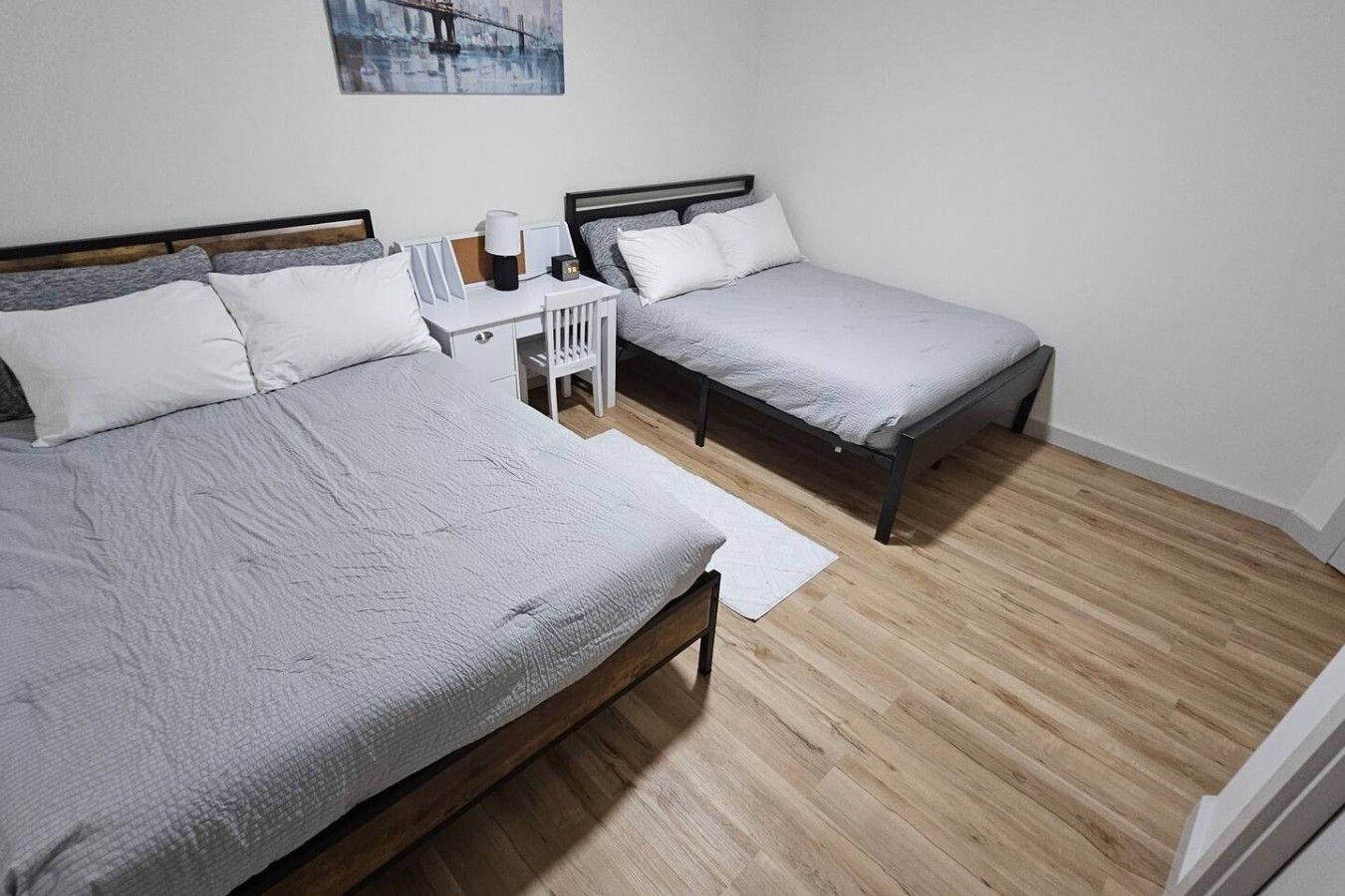 Una habitación con dos camas individuales, una mesita de noche blanca con una lámpara y un cuadro en la pared.