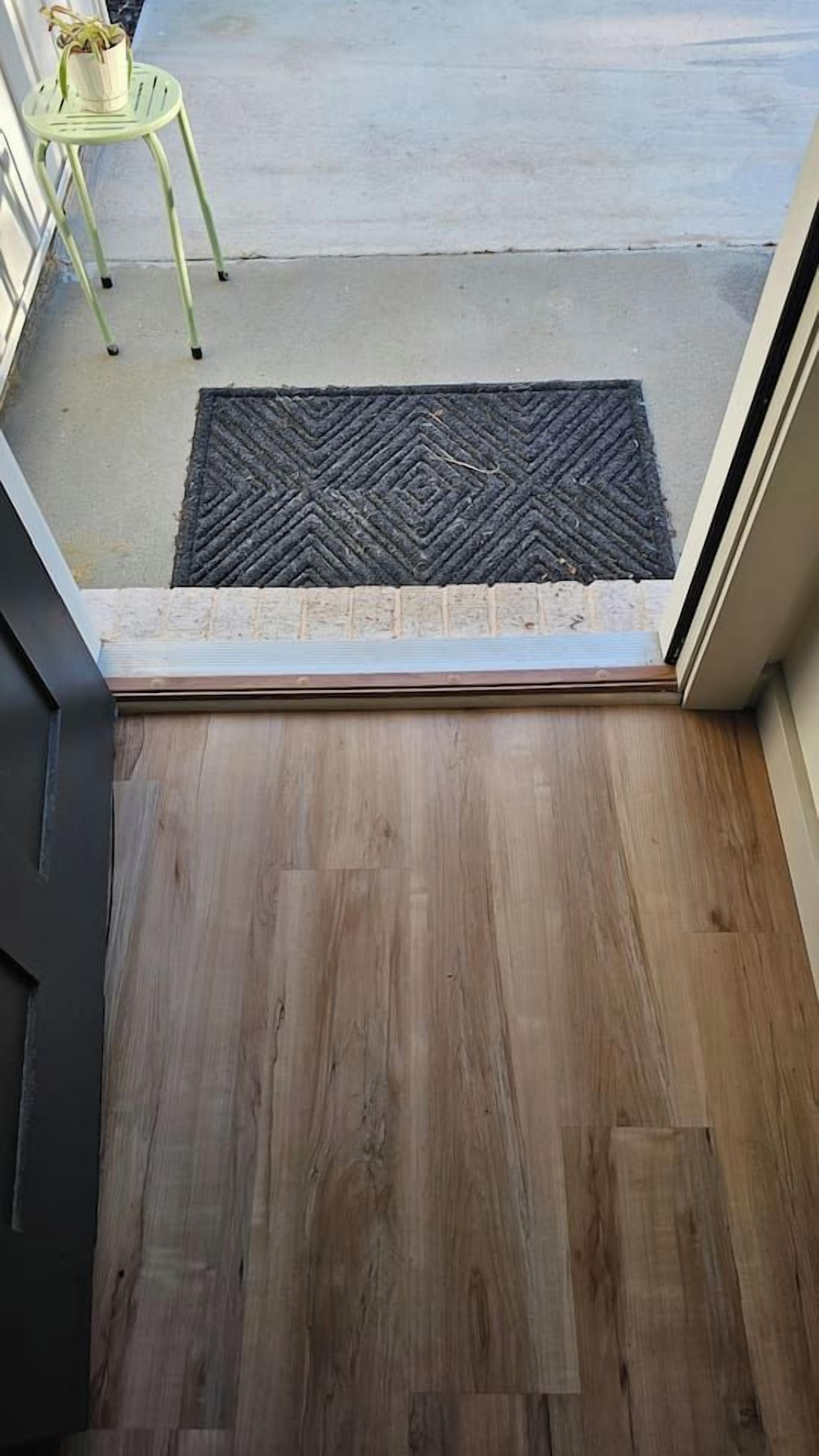 A wooden floor leading to a concrete patio with a doormat.