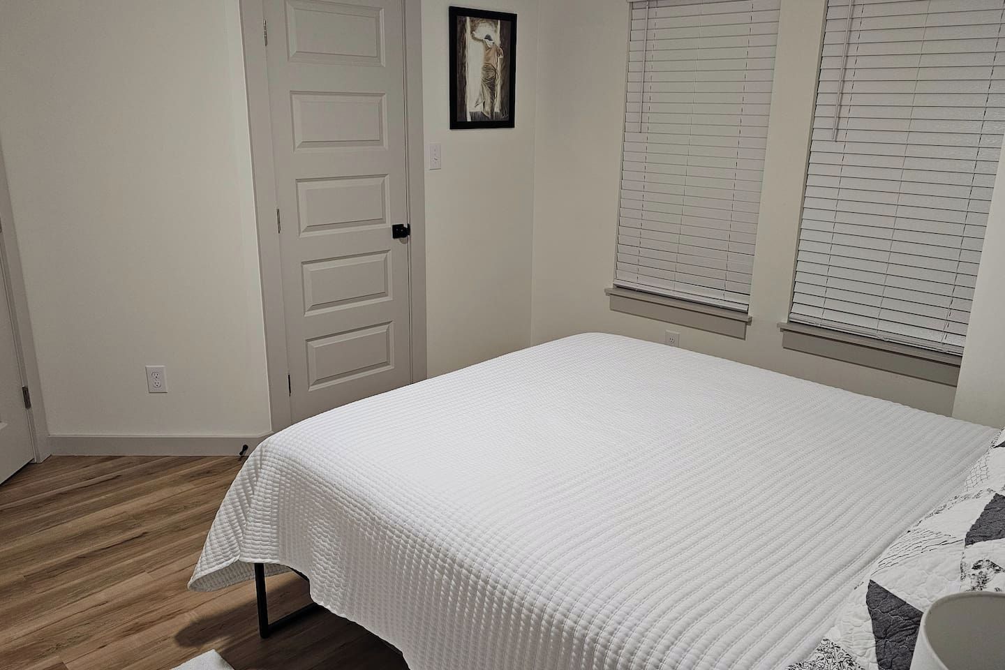 A bedroom with a bed, a door, and a window with blinds.