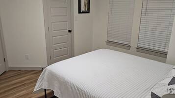 A bedroom with a bed, a door, and a window with blinds.