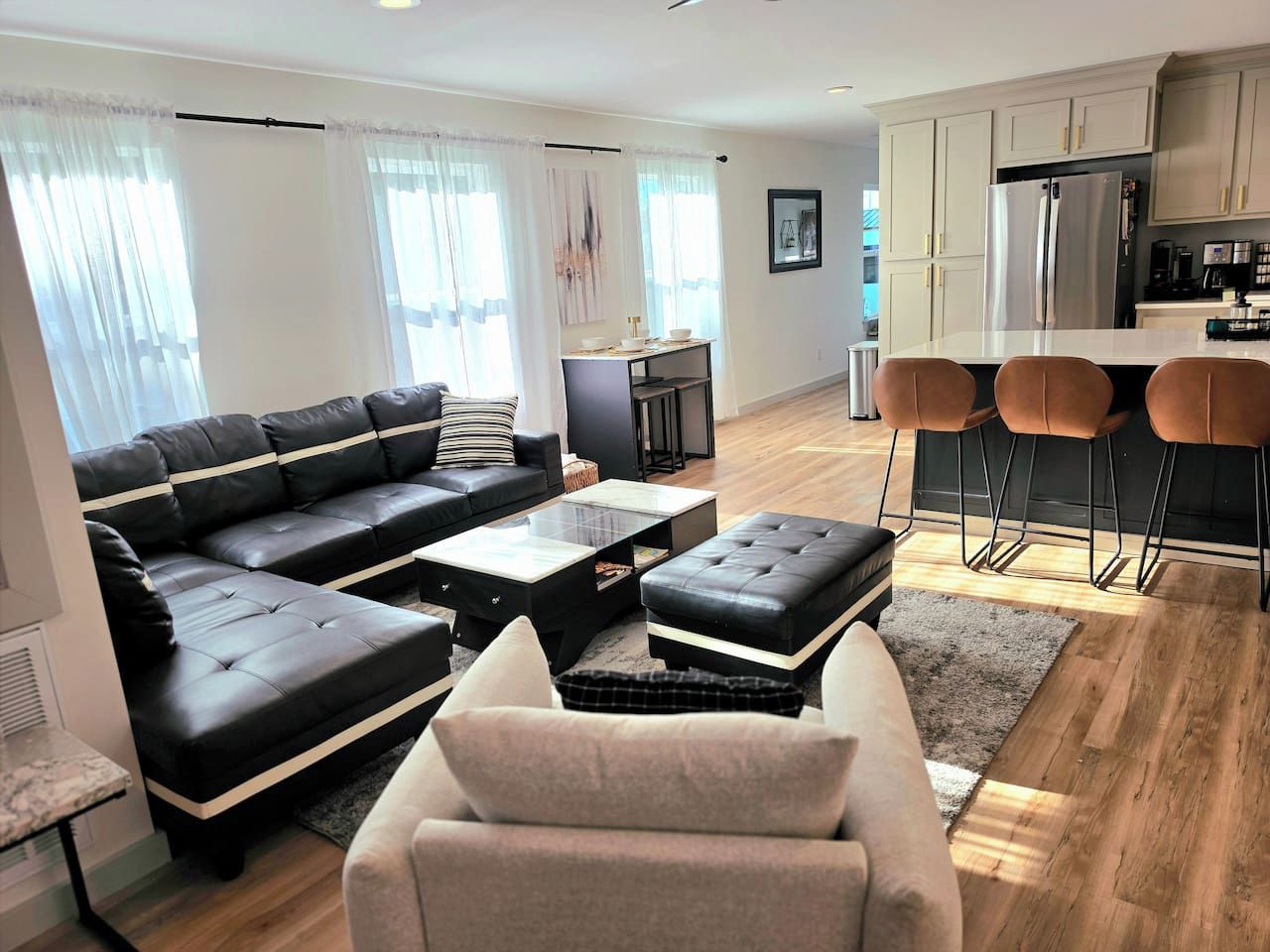 Una sala de estar moderna con sofá, reposapiés, mesa de centro y un comedor con sillas.