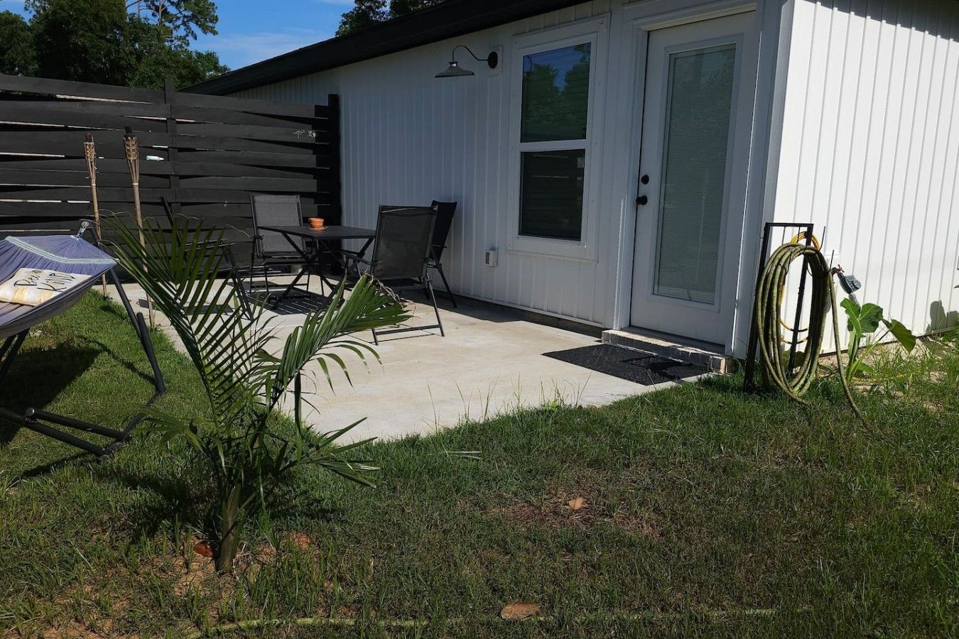 Une terrasse avec une table et des chaises, un petit jardin et une porte avec une fenêtre.