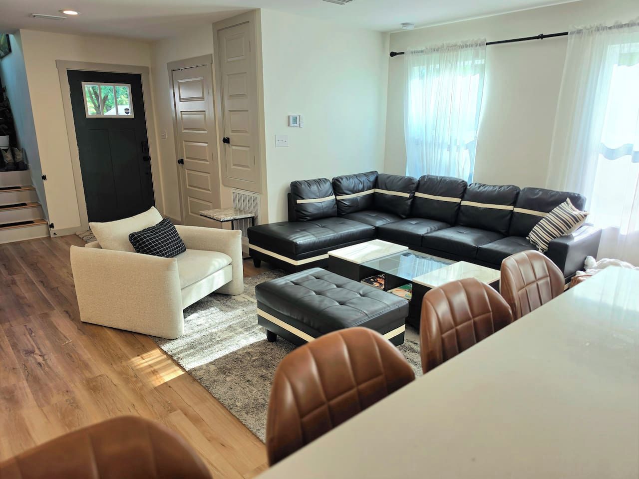 Una sala de estar con un sofá seccional, un sillón blanco y una mesa de comedor con sillas.