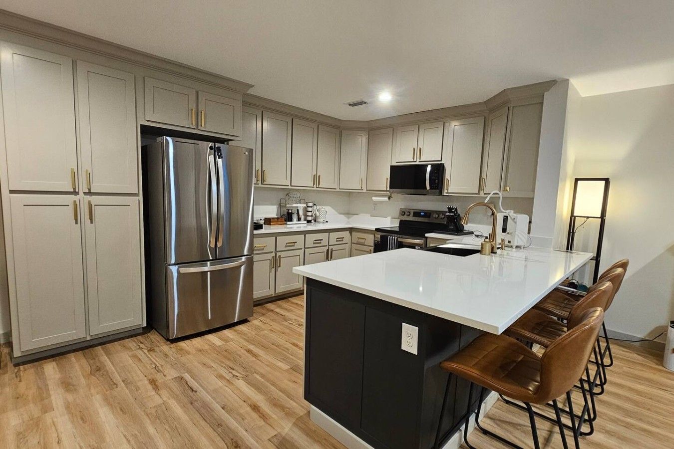 A modern kitchen with stainless steel appliances, a central island with bar stools, and light-colored cabinetry.
