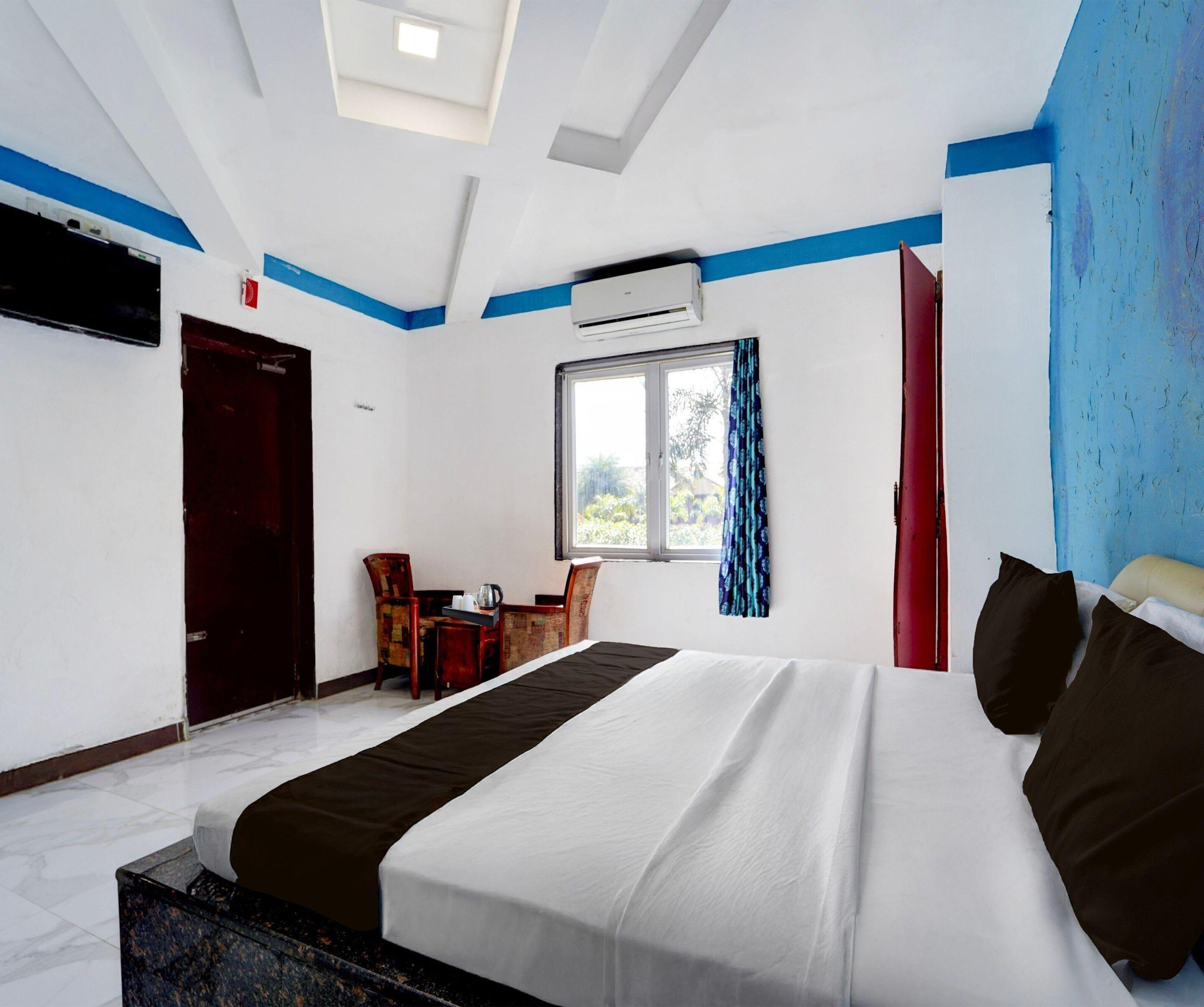 Habitación de hotel con cama, escritorio, sillas, ventana con cortinas, unidad de aire acondicionado y tragaluz.