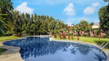 A swimming pool with a curved edge, surrounded by greenery and a clear sky.