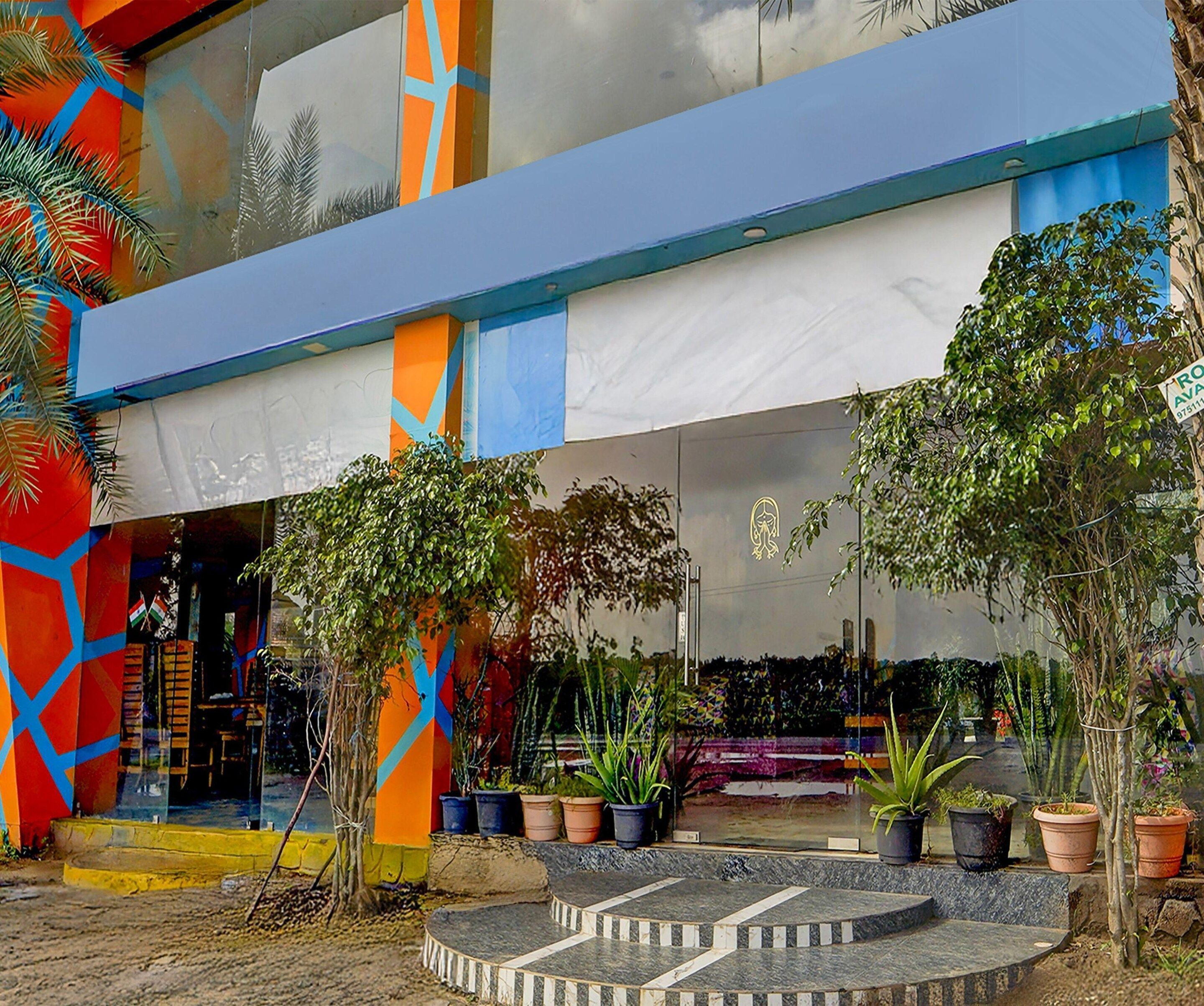 A colorful building with a blue awning, potted plants, and a tiled entrance area.