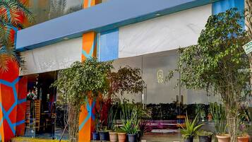 A colorful building with a blue awning, potted plants, and a tiled entrance area.