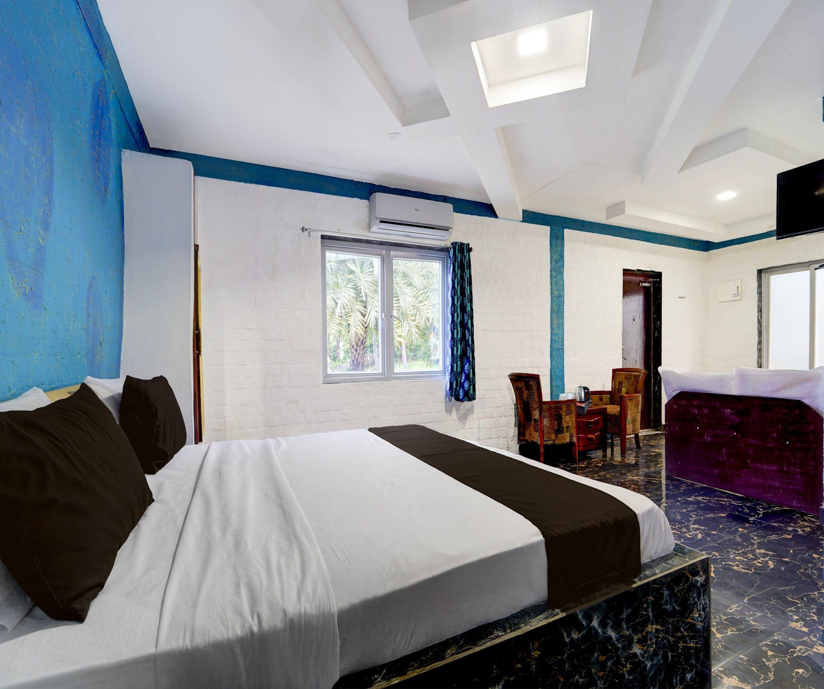 Habitación de hotel con cama, ventana con cortinas, zona de estar con sillas y televisión en la pared.