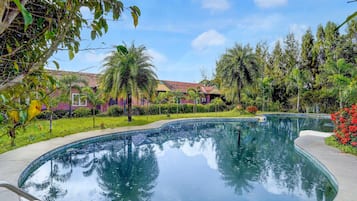 A swimming pool with a clear view of the surrounding greenery and a building with a tiled roof.