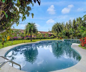 Piscina com vista clara para a vegetação ao redor e um edifício com telhado em azulejos.