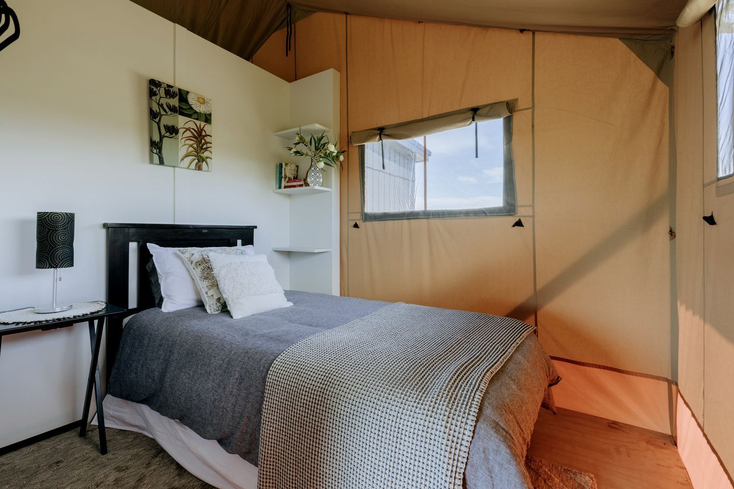 A tented room with a bed, a bedside table, a lamp, and a window.