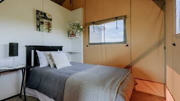 A tented room with a bed, a bedside table, a lamp, and a window.
