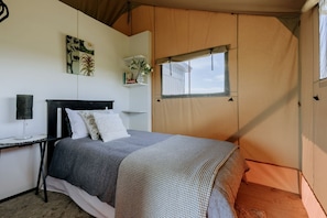 A tented room with a bed, a bedside table, a lamp, and a window.
