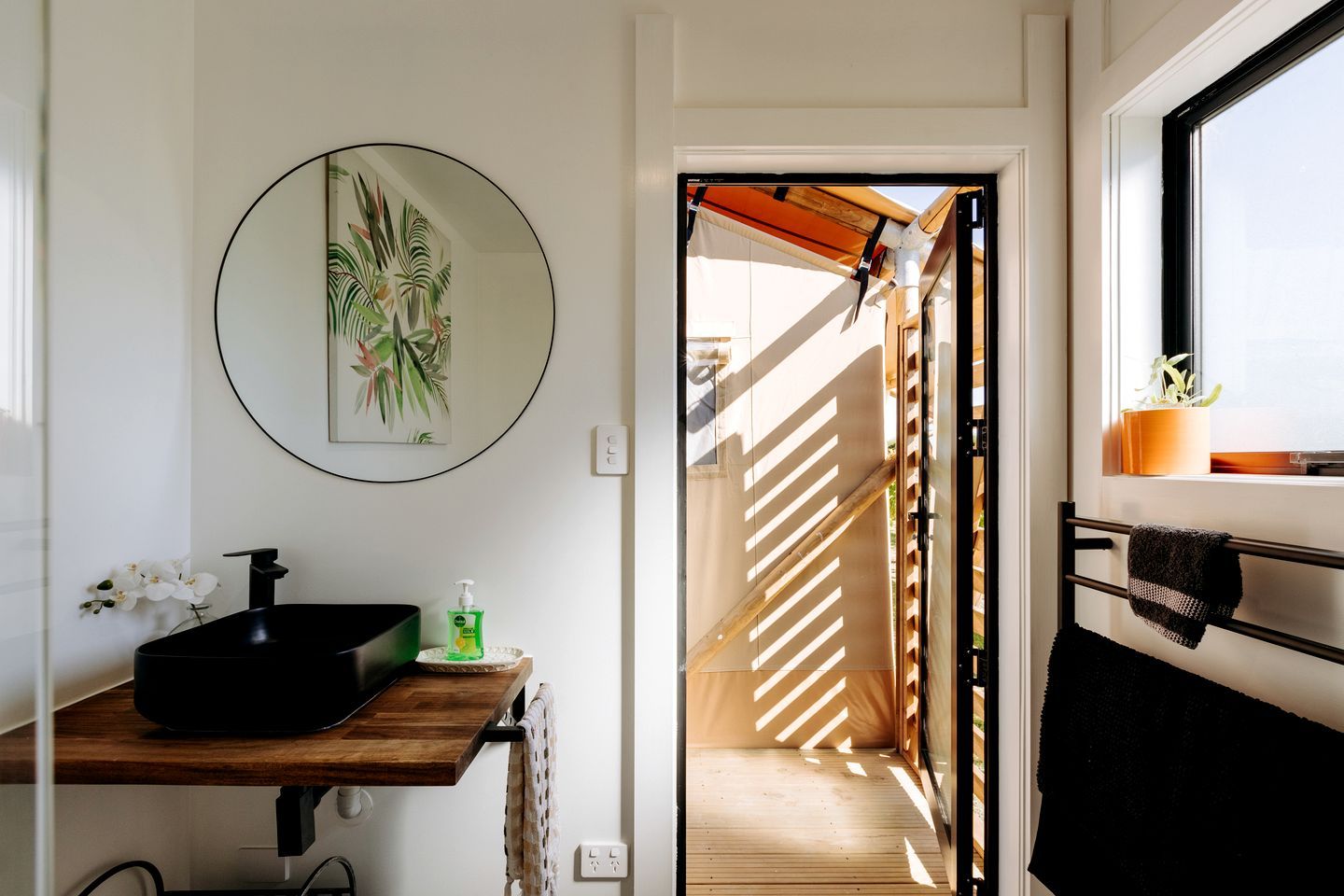 A bathroom with a black sink, a round mirror, and a framed plant.