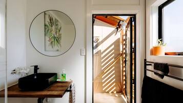 A bathroom with a black sink, a round mirror, and a framed plant.