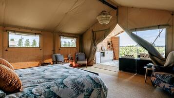 A tented accommodation with a bed, seating area, and a view of the outdoors.