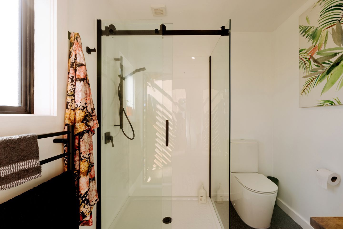 Une cabine de douche fermée par des parois en verre, dotée d’un pommeau de douche à main, de toilettes et d’un porte-serviettes avec une serviette.