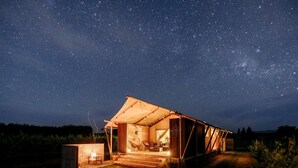 Una struttura a forma di tenda con un cielo stellato visibile attraverso gli spazi aperti, un piccolo braciere e un sentiero che conduce all'ingresso.
