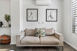 A neutral-toned sofa with a floral pillow, two framed artworks on the wall, a potted plant, and a vintage trunk. -  Casa Dias  Scenic Mountain Views, Unbeatable City Access (Cape Town)