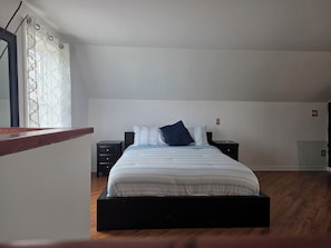 Ein Schlafzimmer mit einem Bett, zwei Nachttischen, einem Fenster mit Vorhängen und einem Holzboden.
