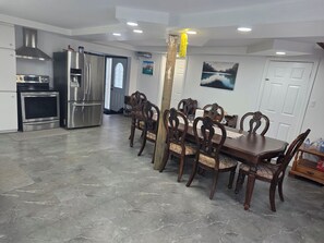 A modern kitchen with stainless steel appliances, a dining area with wooden chairs, and a large window with a view.