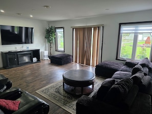 A modern living room with a flat-screen TV, a large sofa, a coffee table, and a dining area with a table and chairs.
