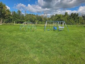 A playground with a swing set and a climbing structure in a grassy field.