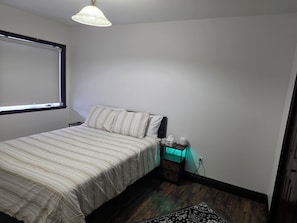 Une chambre à coucher avec un lit, une table de chevet, une lampe et une fenêtre.