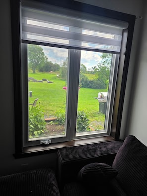 Ein Fenster mit Blick auf eine grüne Außenanlage, eine Bank und ein Stuhl in einem Zimmer.
