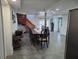 Un vaste espace dédié à la salle à manger, avec une table et des chaises en bois, un escalier et une cuisine moderne dotée de meubles blancs.