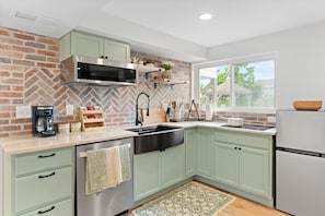 A modern kitchen with green cabinets, a stainless steel range hood, and a window with a view of greenery.