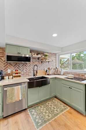 A kitchen with green cabinets, a brick backsplash, a built-in oven, and a window with a view of the outdoors.