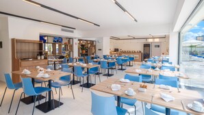 Uma área de refeições moderna com várias mesas e cadeiras, espaço de cozinha e vista para o exterior.