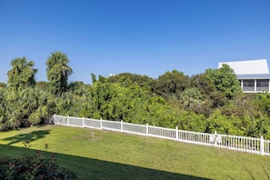 A well-maintained grassy area with a white fence, dense greenery, and a building with a white roof in the background. - Marsh View Condo Steps to Beach Boardwalk - Pet Friendly (Saint Helena Island)