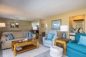 A living room with a sofa, armchairs, a coffee table, and a dining area with a table and chairs. - Marsh View Condo Steps to Beach Boardwalk - Pet Friendly (Saint Helena Island)