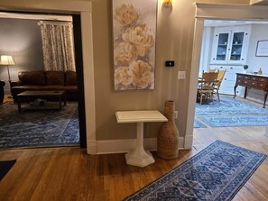 Een kamer met een houten vloer, een witte bijzettafel, een vaas en een schilderij van bloemen.