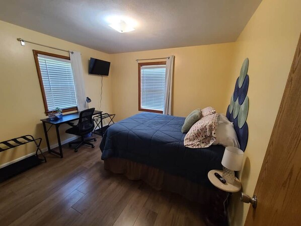 A bedroom with a bed, a desk, a chair, and two windows with blinds.