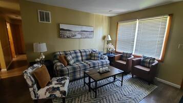A living room with a sofa, armchair, coffee table, and a painting on the wall.