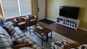 Een woonkamer met een bank, fauteuils, een salontafel, een televisie en een deur.