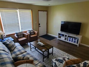Una sala de estar con sofá, sillones, una mesa de centro, televisor y una puerta.