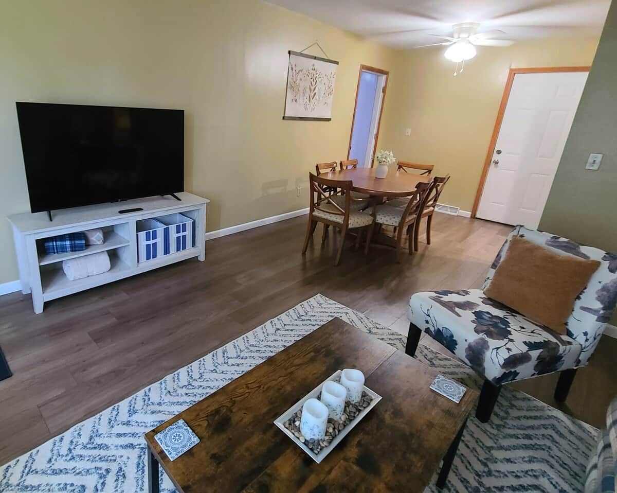 Uma sala de estar com televisão, mesa de jantar e poltrona estampada.