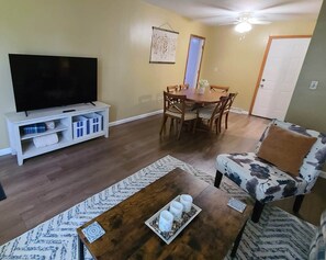 A living room with a television, a dining table, and a floral armchair.