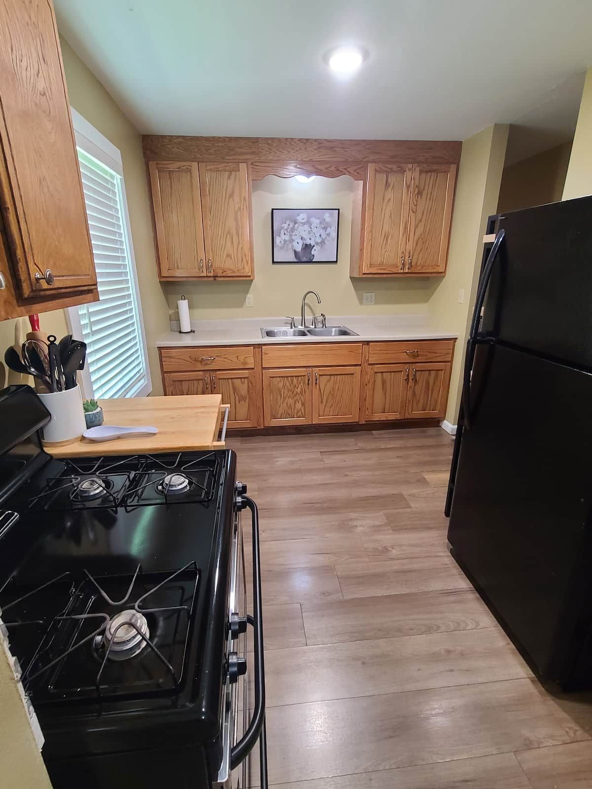 A kitchen with wooden cabinets, a black stove, a sink, and a refrigerator.